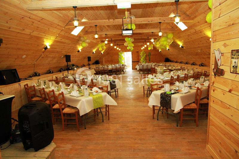 Salle en bois décorée avec des ballons verts, tables dressées pour un repas avec nappes blanches et chaises en bois.
