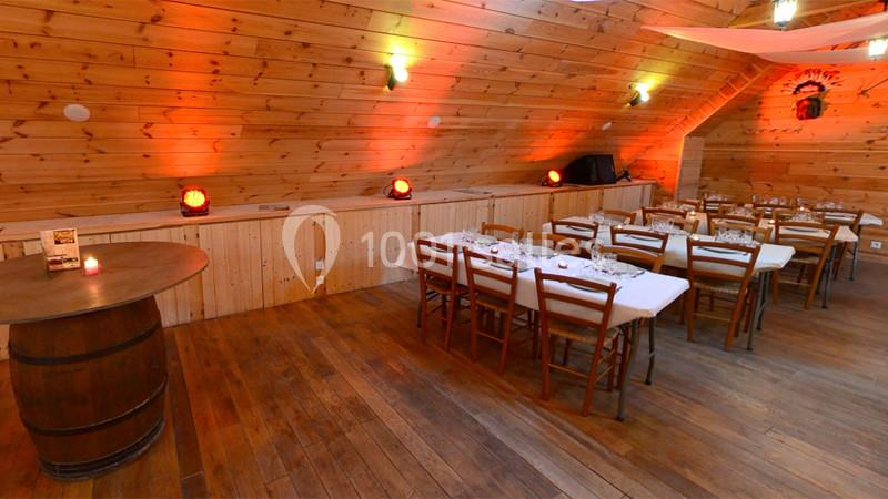 Salle en bois avec tables dressées, chaises en bois, éclairage chaleureux et décor rustique.