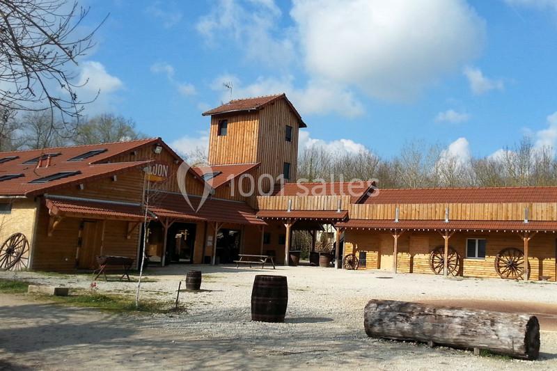 Bâtiment en bois de style ranch avec une tour centrale, des roues décoratives et un ciel partiellement nuageux.
