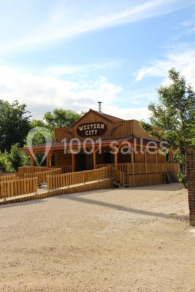Bâtiment en bois de style western avec une enseigne ’Western City’, entouré d'arbres et d'une clôture en bois.