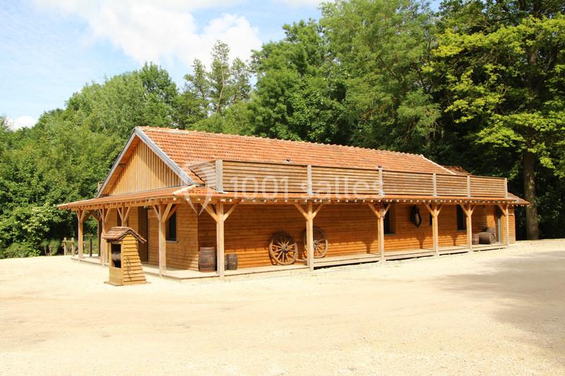 Bâtiment en bois avec toit en tuiles, entouré d'arbres, comportant une terrasse et des éléments décoratifs rustiques.