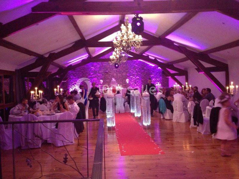 Salle de réception décorée pour un événement, avec tables dressées, chandeliers et éclairage violet.