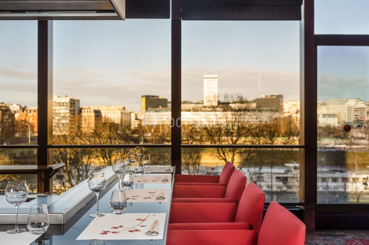 Salle à manger moderne avec chaises rouges et vue panoramique sur une ville au coucher du soleil.