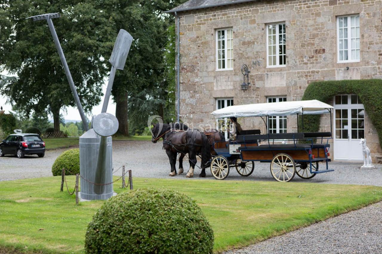 Calèche tirée par deux chevaux stationnée devant un bâtiment en pierre, avec une sculpture métallique au premier plan.