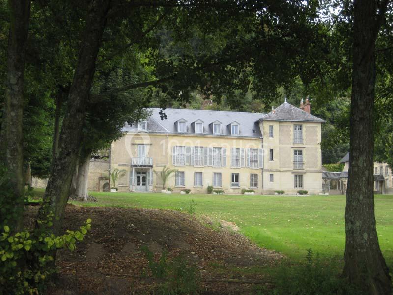 Grande maison en pierre à deux étages, entourée d'arbres et donnant sur une pelouse verdoyante.