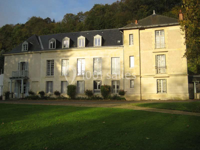Façade d'un grand bâtiment ancien en pierre, entouré de pelouse et d'arbres en arrière-plan.
