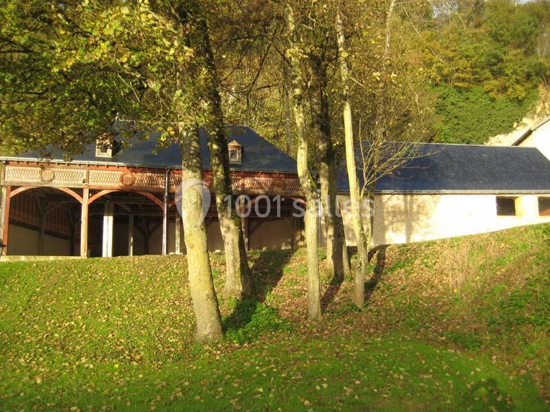 Bâtiment à colombages avec toit en ardoise, entouré d'arbres et d'une pelouse ensoleillée.