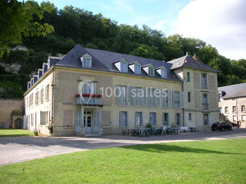 Bâtiment ancien à deux étages avec volets bleus, situé devant une pelouse et entouré de végétation.