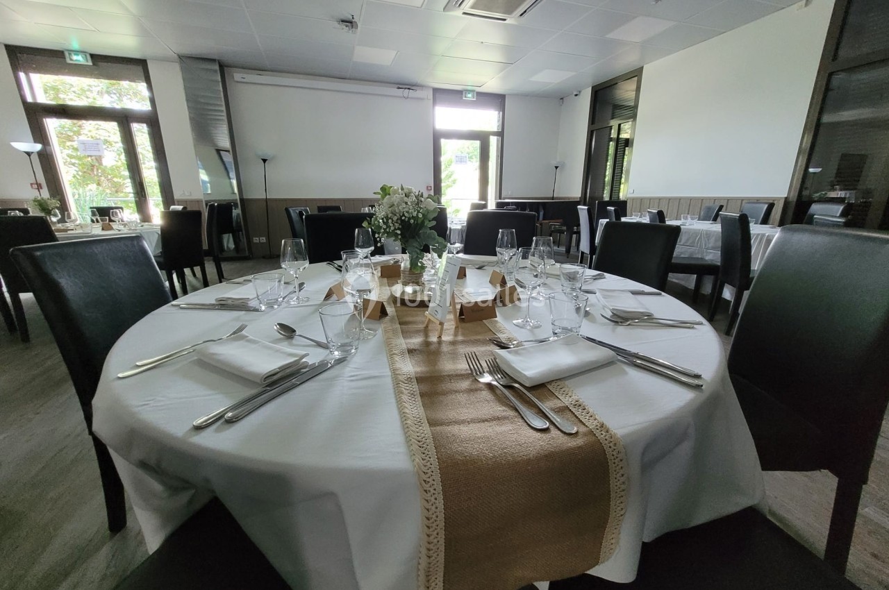 Salle de réception avec une table ronde dressée élégamment, nappes blanches et décoration florale centrale.