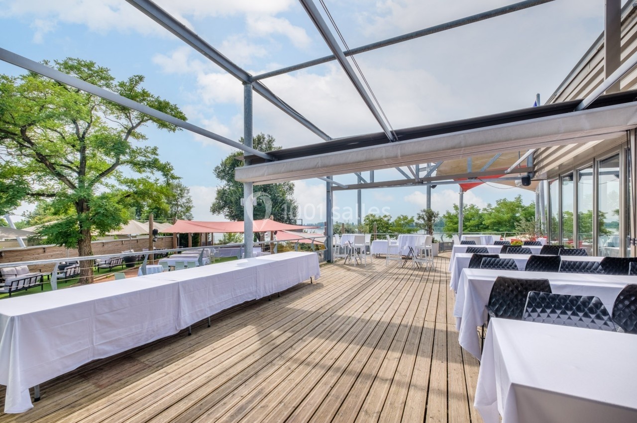 Terrasse en bois aménagée avec des tables dressées, entourée de verdure et partiellement abritée par une structure…