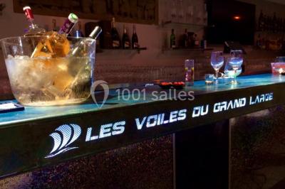 Foule dans une discothèque éclairée par des lumières bleues, avec une ambiance festive et un panneau lumineux au premier…