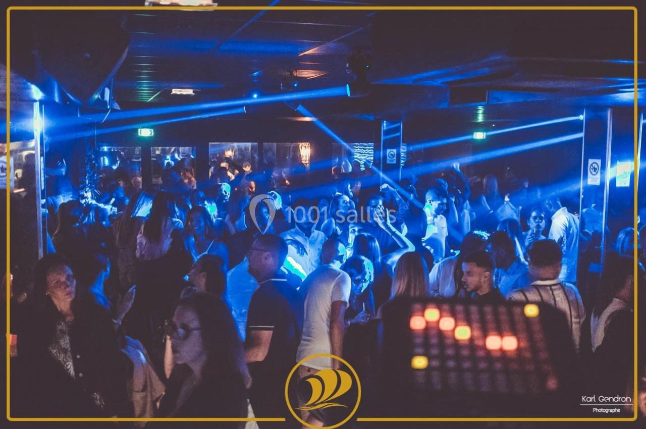 Foule dans une discothèque éclairée par des lumières bleues, avec une ambiance festive et un panneau lumineux au premier…