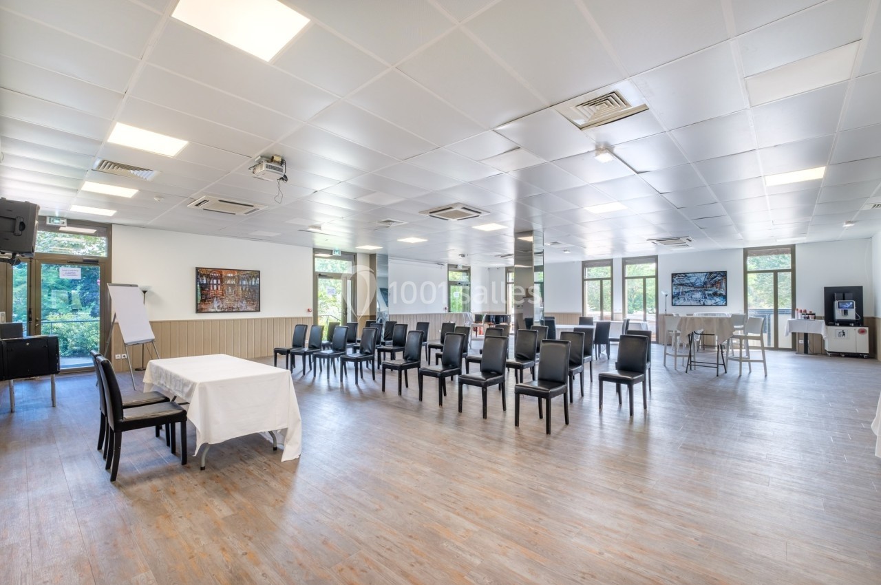 Salle lumineuse avec chaises alignées, tables dressées et équipements pour réunion, vue sur des fenêtres donnant sur l…