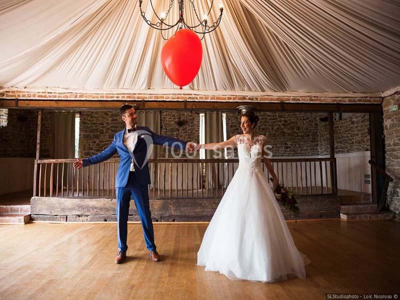 Un couple en tenue de mariage se tient la main sous un plafond drapé, avec un ballon rouge flottant au-dessus.