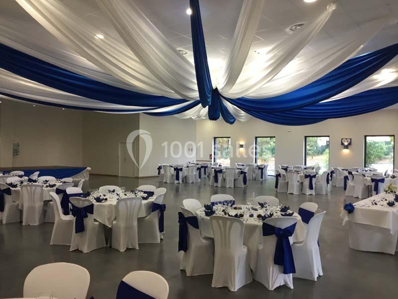 Salle de réception décorée avec des nappes blanches, des rubans bleus et un plafond drapé de tissus bleu et blanc.