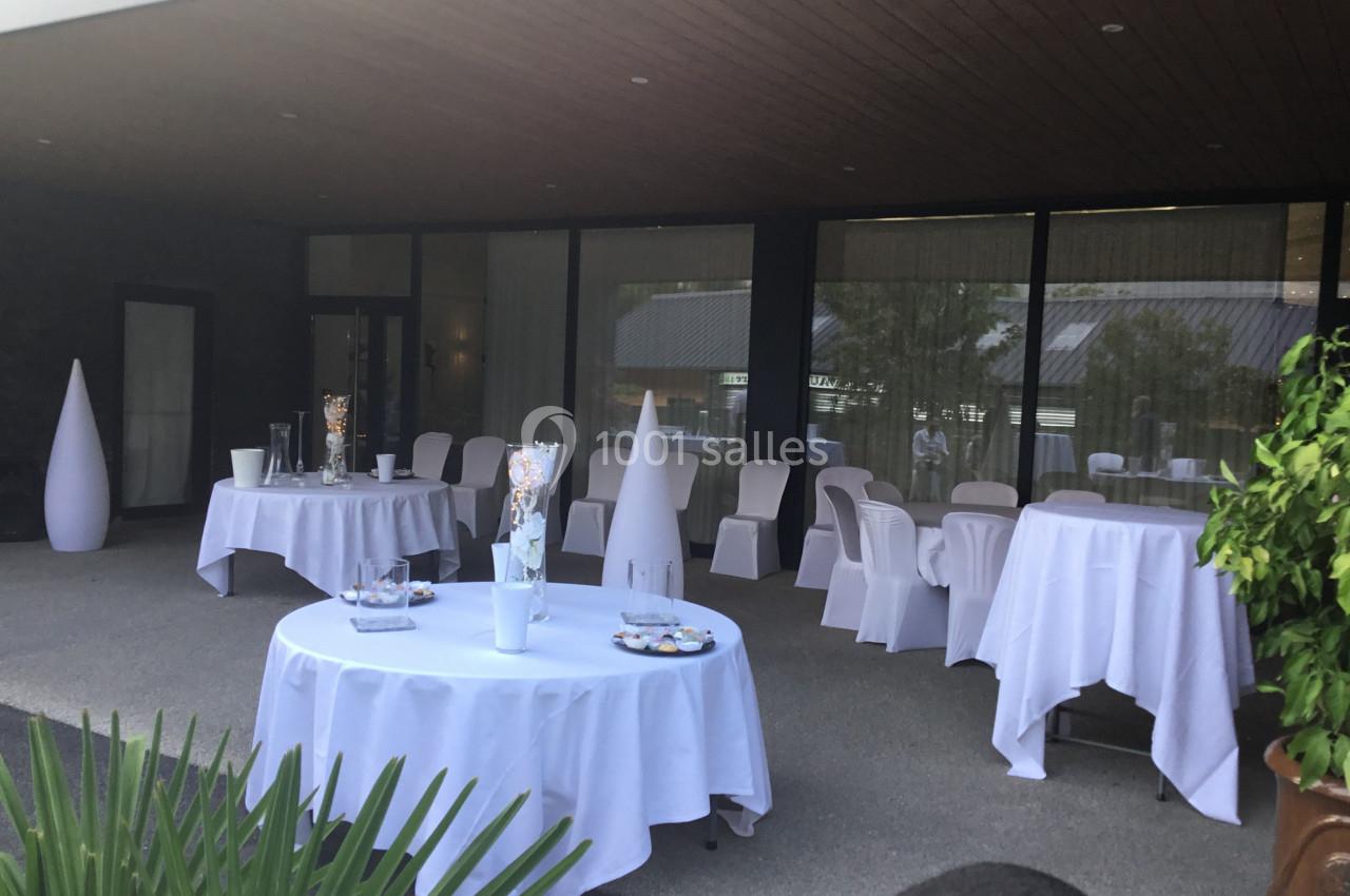 Terrasse aménagée pour un événement avec tables rondes et chaises recouvertes de nappes blanches.