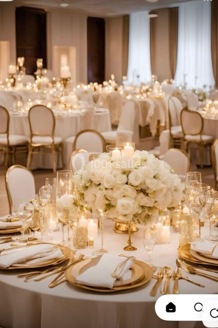Salle de réception élégante avec tables décorées de fleurs blanches, bougies et vaisselle raffinée.