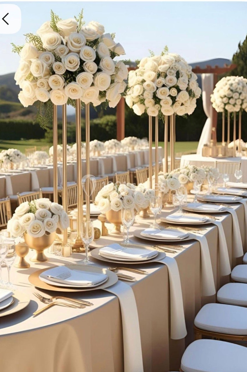 Tables élégamment dressées en extérieur avec nappes beiges, vaisselle raffinée et centres de table ornés de roses blanches.