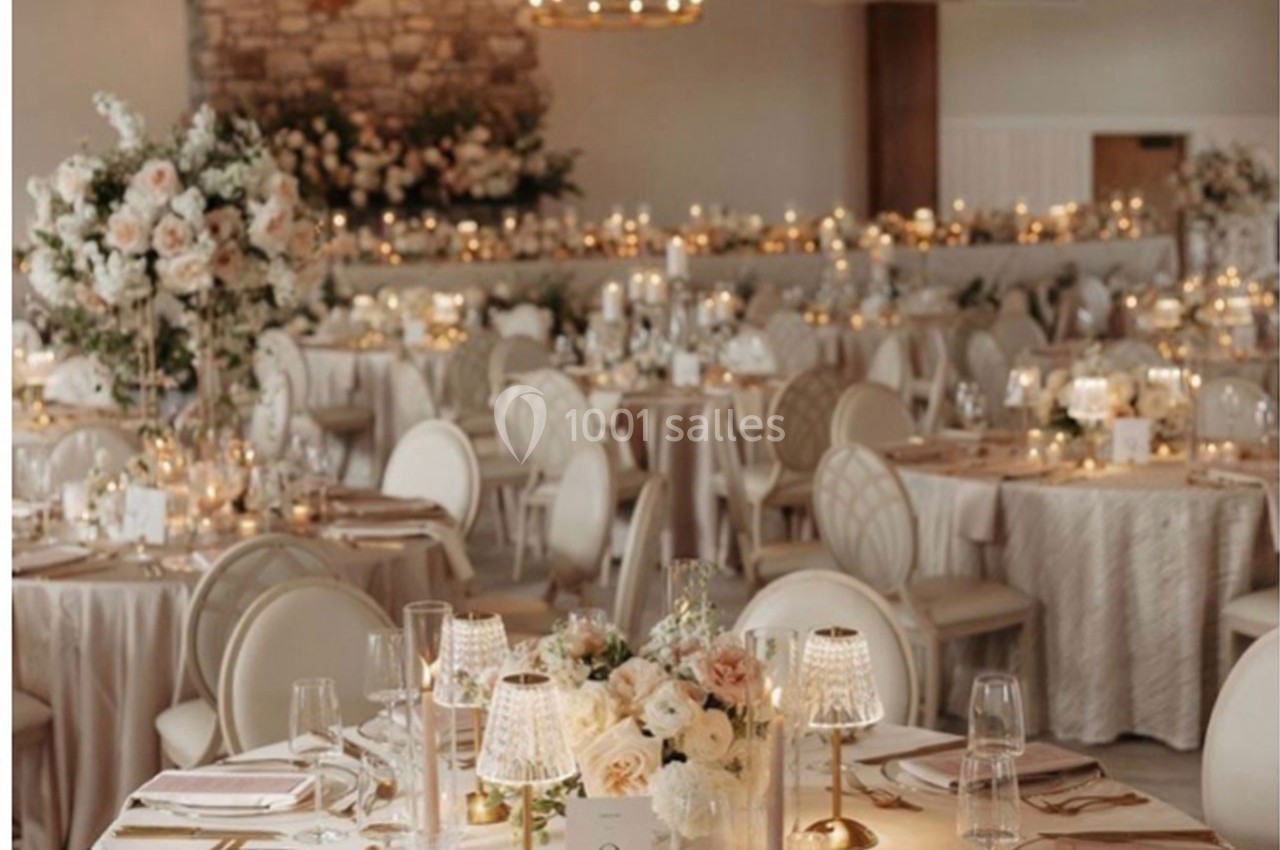Salle de réception élégante décorée de fleurs blanches, bougies et tables dressées pour un événement formel.