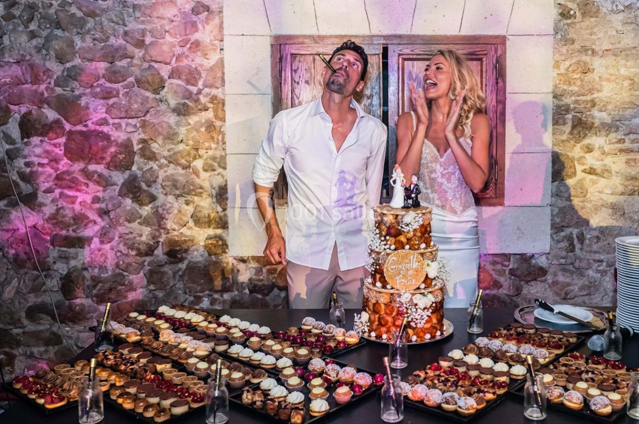 Location salle Gémenos (Bouches-du-Rhône) - Moulin de Gemenos #6 Un couple souriant devant une pièce montée et des plateaux de desserts, dans une salle en pierre éclairée.