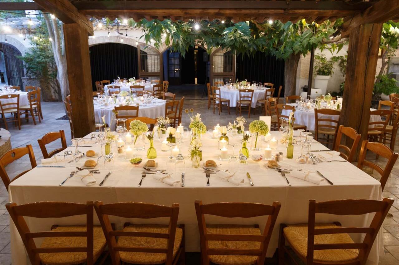 Location salle Gémenos (Bouches-du-Rhône) - Moulin de Gemenos #19 Grande table dressée pour un dîner en extérieur, entourée de chaises en bois, sous une pergola décorée de feuillage.