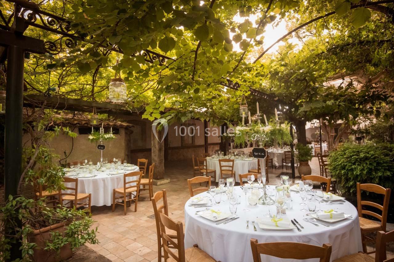 Location salle Gémenos (Bouches-du-Rhône) - Moulin de Gemenos #11 Tables rondes dressées avec nappes blanches sous une pergola couverte de feuillage dans un jardin ensoleillé.