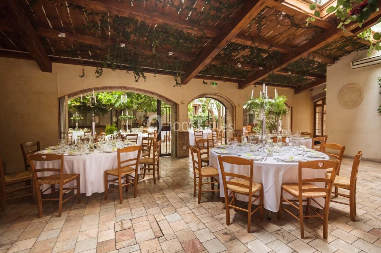 Location salle Gémenos (Bouches-du-Rhône) - Moulin de Gemenos #14 Salle de réception lumineuse avec tables rondes dressées, chaises en bois et plafond décoré de végétation suspendue.