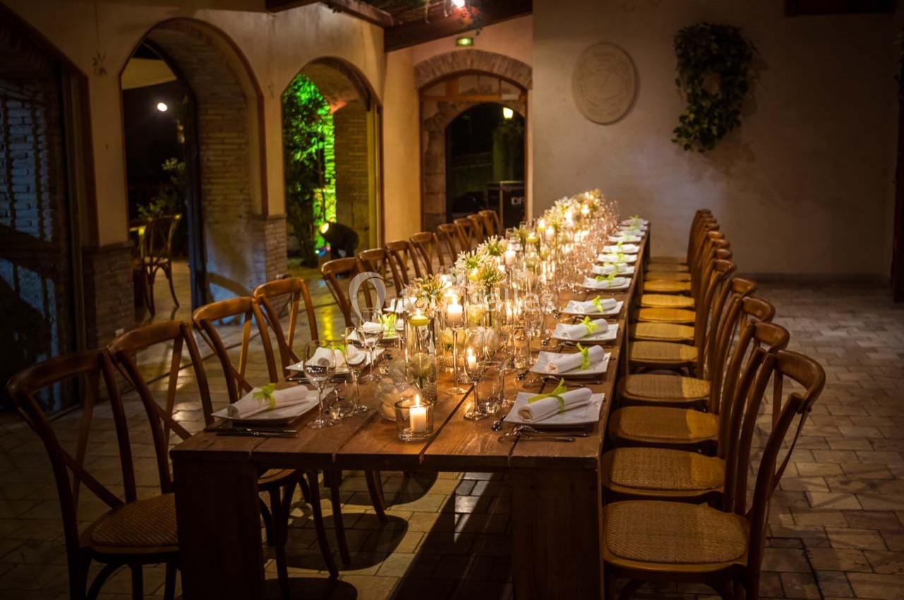 Location salle Gémenos (Bouches-du-Rhône) - Moulin de Gemenos #29 Grande table en bois décorée de bougies et de serviettes blanches, entourée de chaises dans une salle éclairée…