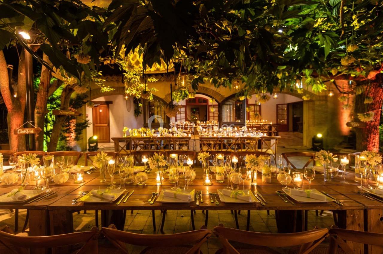Location salle Gémenos (Bouches-du-Rhône) - Moulin de Gemenos #32 Tables en bois décorées de bougies et de fleurs jaunes, disposées dans un jardin éclairé pour un dîner en soirée.
