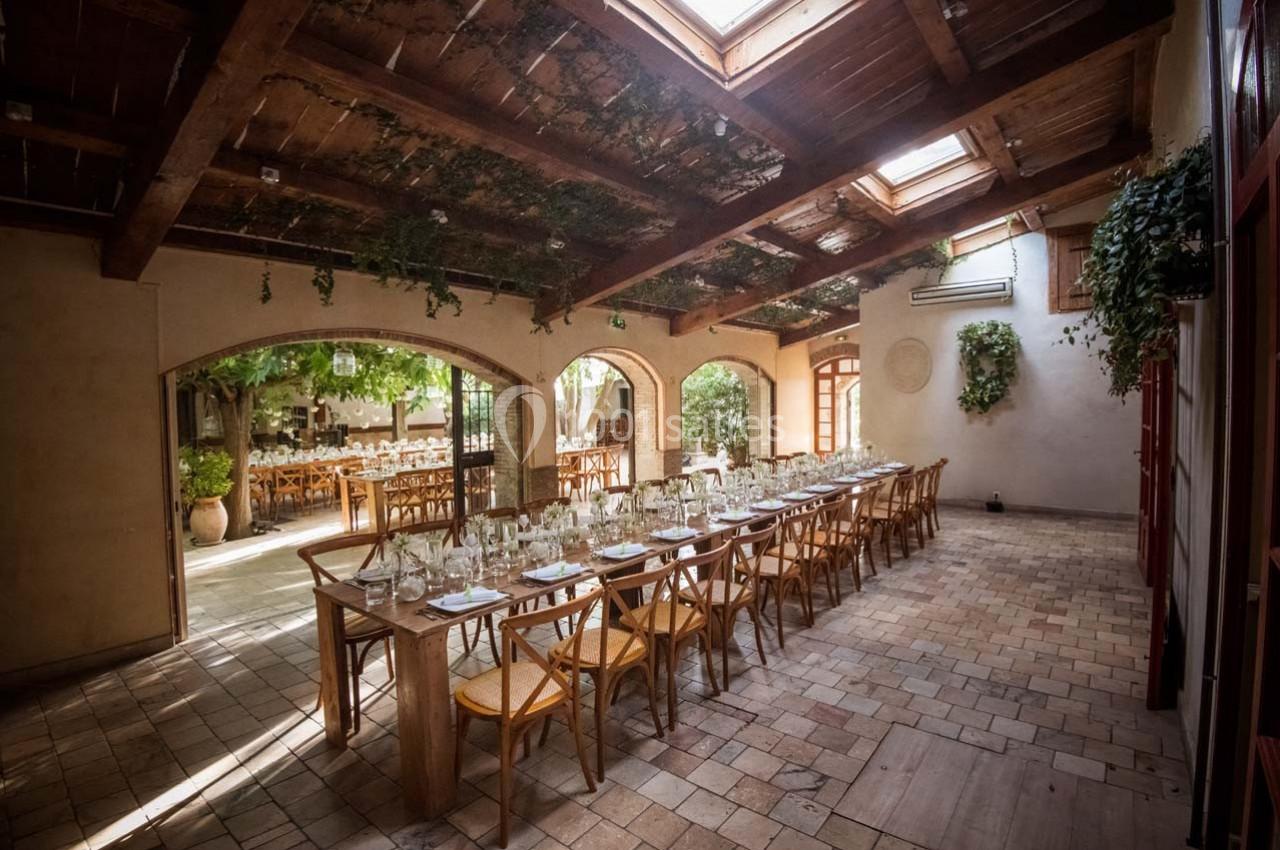 Location salle Gémenos (Bouches-du-Rhône) - Moulin de Gemenos #34 Salle lumineuse avec tables en bois dressées pour un repas, grandes baies vitrées et plantes suspendues.
