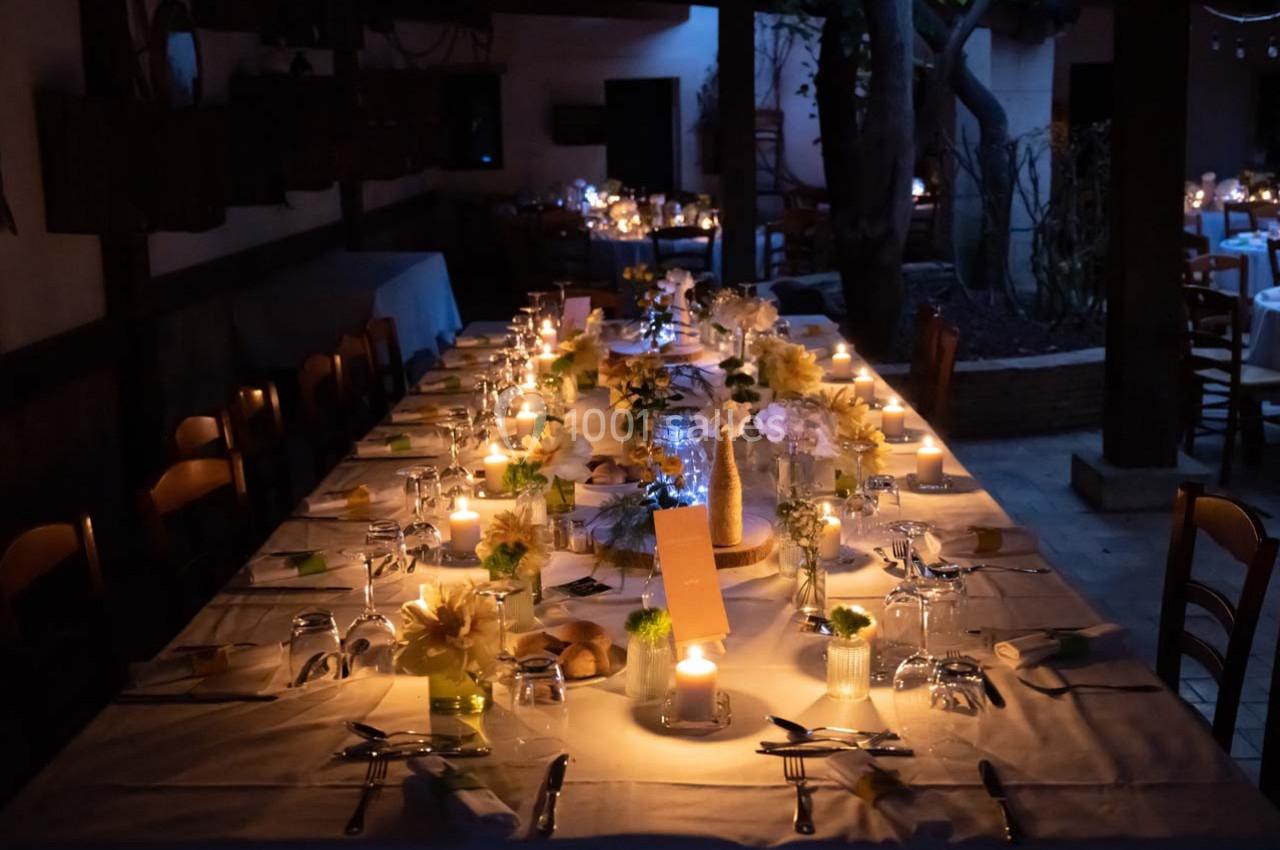 Location salle Gémenos (Bouches-du-Rhône) - Moulin de Gemenos #42 Grande table dressée pour un dîner, éclairée par des bougies, avec des fleurs et des couverts disposés soigneusement.