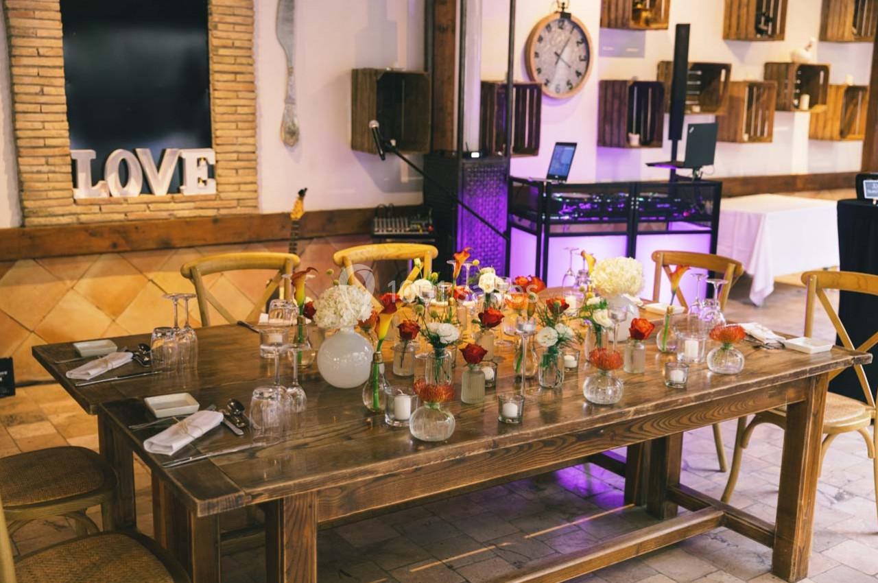 Location salle Gémenos (Bouches-du-Rhône) - Moulin de Gemenos #46 Table en bois décorée de fleurs, bougies et vaisselle, dans une salle avec murs en briques et éléments décoratifs.