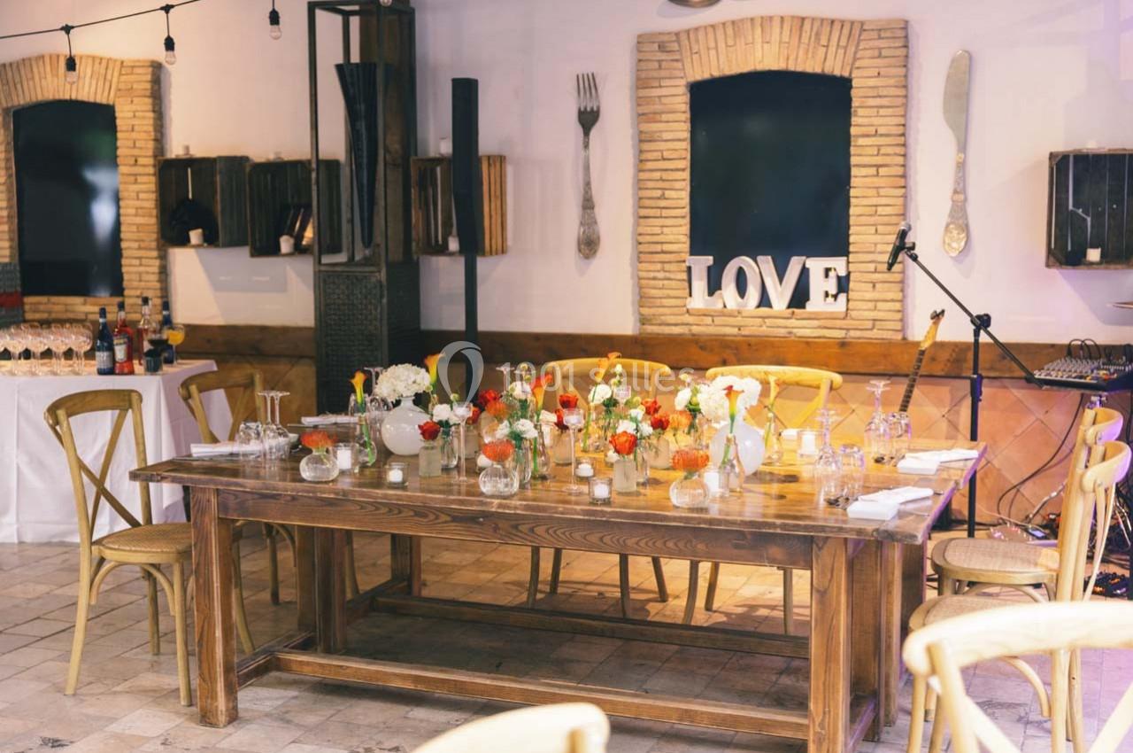 Location salle Gémenos (Bouches-du-Rhône) - Moulin de Gemenos #47 Table en bois décorée de fleurs et bougies dans une salle lumineuse avec des éléments de décoration murale.