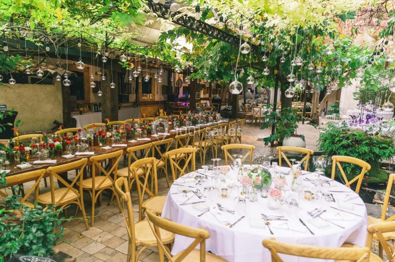 Location salle Gémenos (Bouches-du-Rhône) - Moulin de Gemenos #48 Salle extérieure décorée avec des guirlandes végétales, tables rondes et rectangulaires dressées pour un repas.