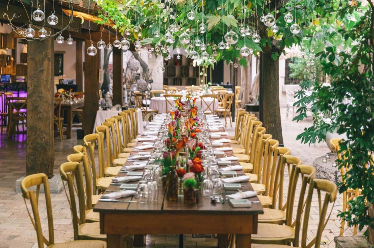 Location salle Gémenos (Bouches-du-Rhône) - Moulin de Gemenos #49 Grande table en bois décorée de fleurs colorées, entourée de chaises, sous un toit végétalisé avec des lumières suspendues.