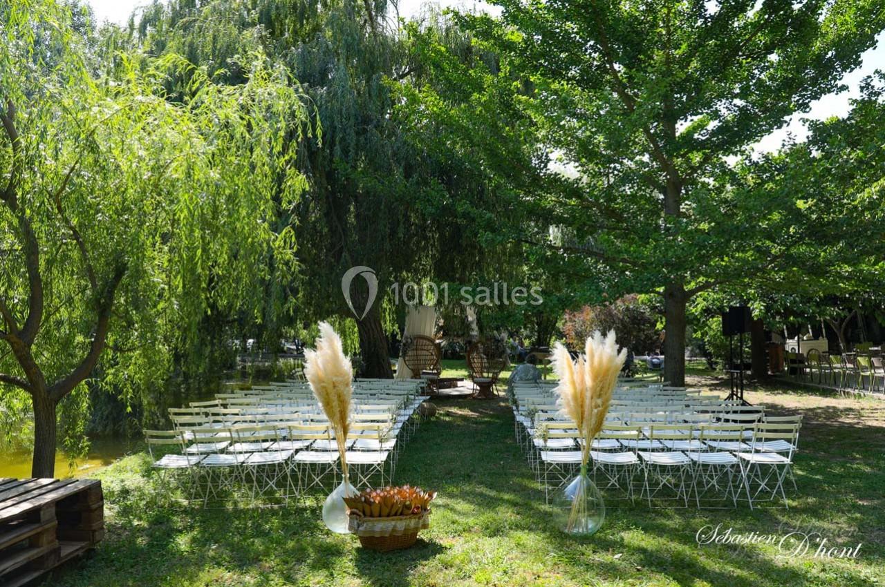Location salle Gémenos (Bouches-du-Rhône) - Moulin de Gemenos #53 Chaises blanches alignées en extérieur sous des arbres, décorées avec des bouquets de pampas, pour un événement.