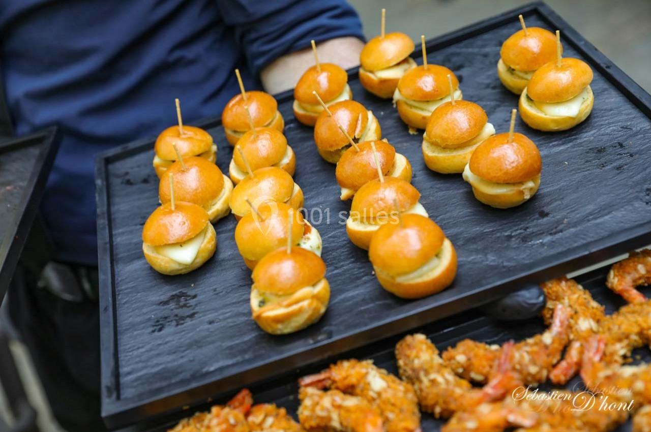 Location salle Gémenos (Bouches-du-Rhône) - Moulin de Gemenos #57 Plateau de mini-burgers dorés et brochettes de crevettes panées disposés sur un support noir.