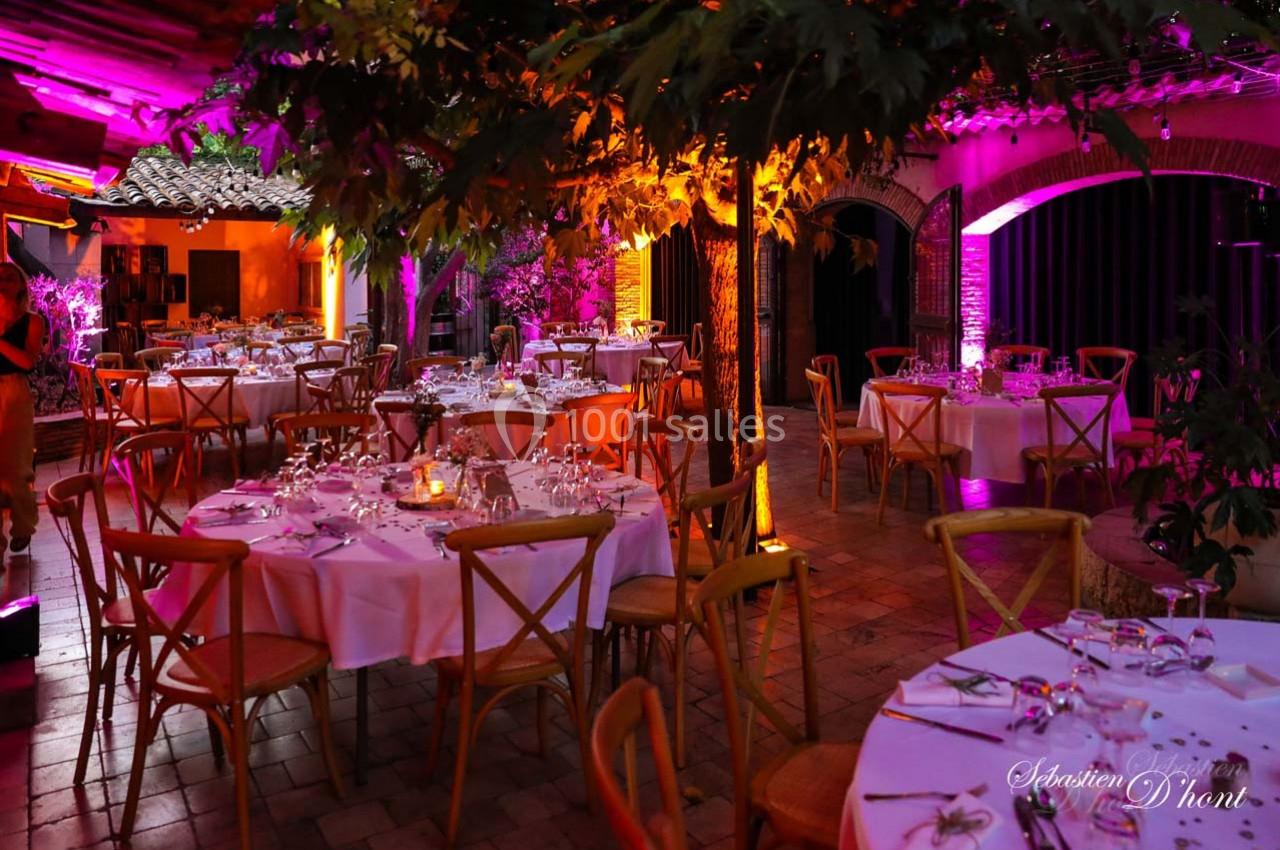 Location salle Gémenos (Bouches-du-Rhône) - Moulin de Gemenos #58 Salle de réception avec tables rondes dressées, éclairage coloré et ambiance chaleureuse sous un toit partiellement ouvert.
