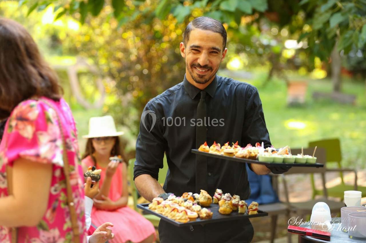 Location salle Gémenos (Bouches-du-Rhône) - Moulin de Gemenos #61 Un serveur souriant présente des plateaux de bouchées apéritives dans un jardin lors d'un événement en plein air.