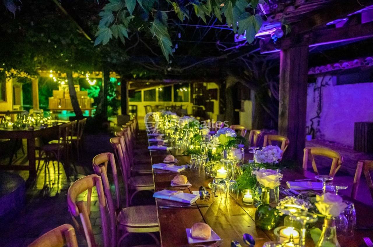 Location salle Gémenos (Bouches-du-Rhône) - Moulin de Gemenos #65 Grande table en bois décorée de fleurs et bougies, installée en extérieur sous des lumières tamisées.
