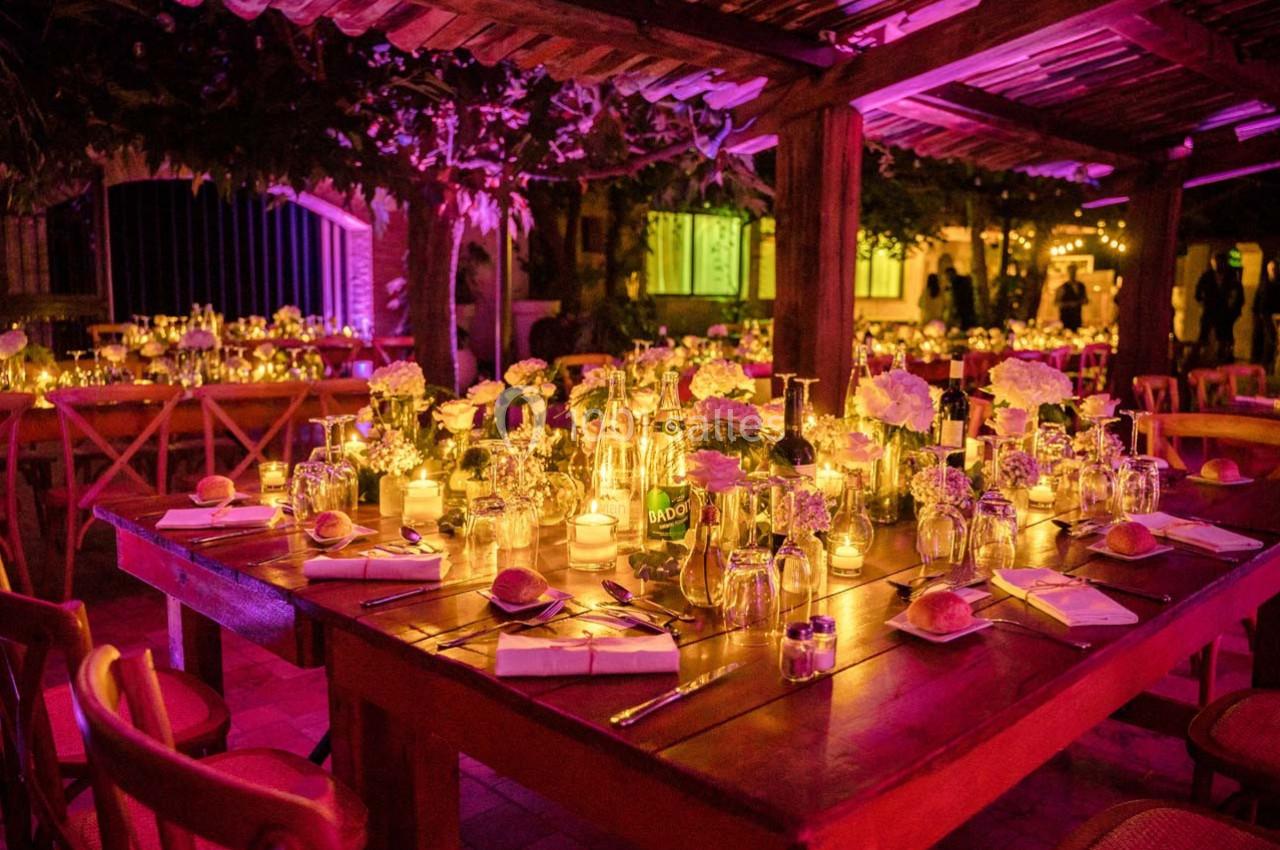 Location salle Gémenos (Bouches-du-Rhône) - Moulin de Gemenos #66 Tables en bois décorées de bougies, fleurs et vaisselle, éclairées par une lumière tamisée dans un cadre extérieur nocturne.