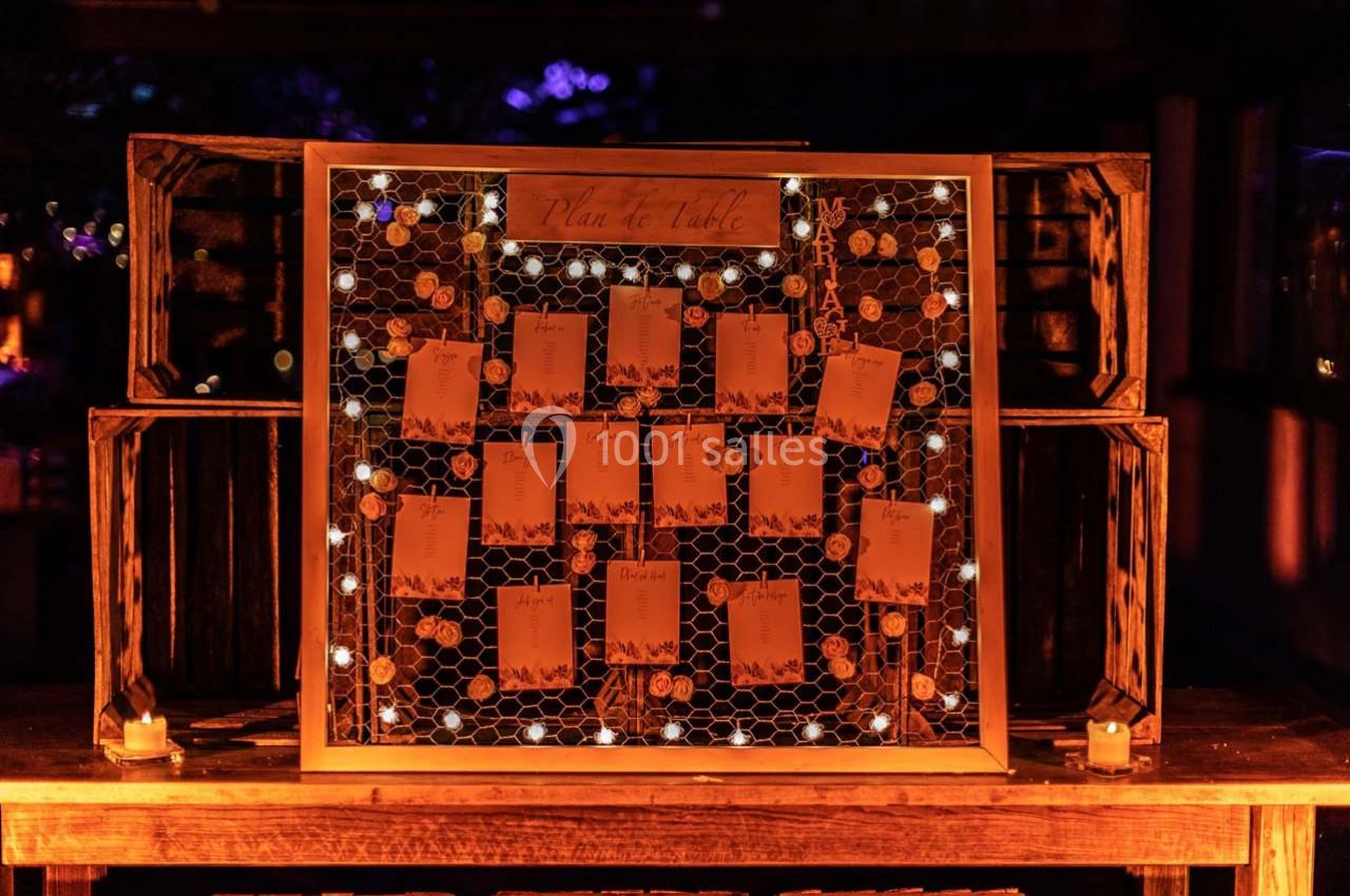 Location salle Gémenos (Bouches-du-Rhône) - Moulin de Gemenos #67 Plan de table éclairé par des guirlandes lumineuses, affiché sur un panneau grillagé avec des cartes suspendues.