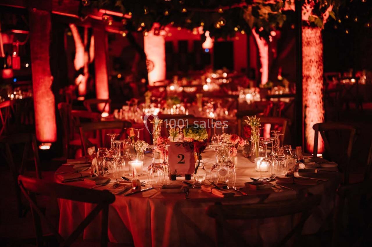 Location salle Gémenos (Bouches-du-Rhône) - Moulin de Gemenos #84 Tables rondes décorées avec des bougies et des fleurs, éclairées par une lumière rouge dans un cadre extérieur nocturne.