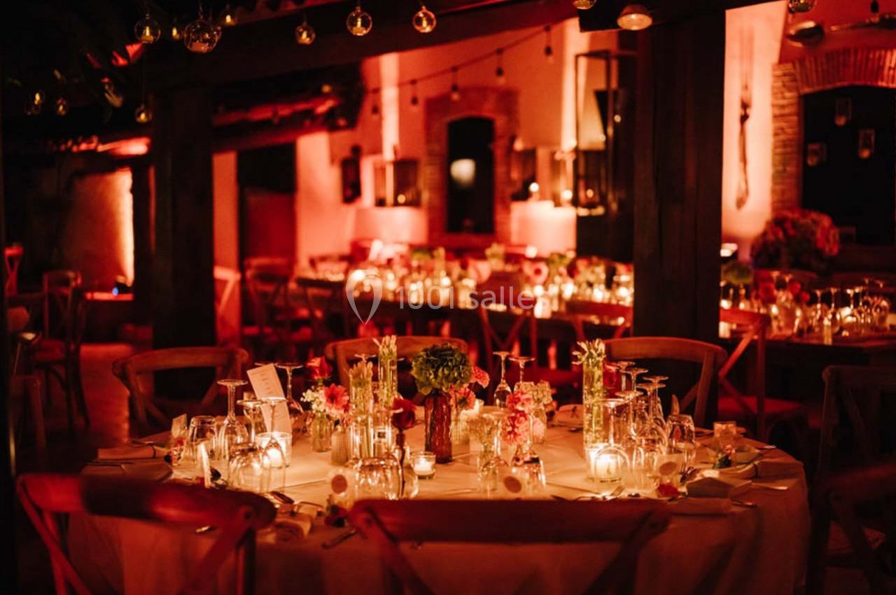 Location salle Gémenos (Bouches-du-Rhône) - Moulin de Gemenos #85 Salle de réception chaleureusement éclairée avec des tables décorées de fleurs, bougies et vaisselle élégante.