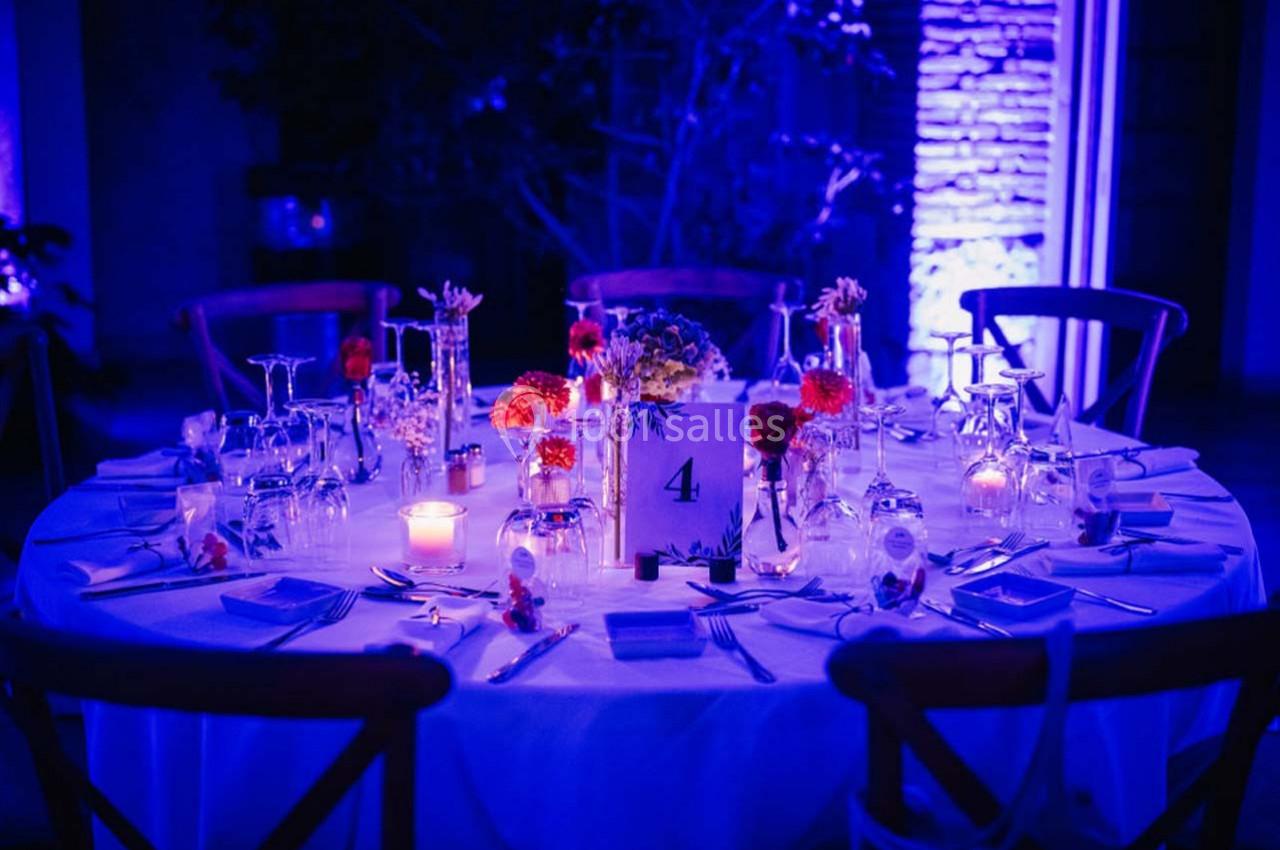 Location salle Gémenos (Bouches-du-Rhône) - Moulin de Gemenos #87 Table ronde décorée pour un dîner, avec bougies, fleurs colorées et vaisselle, éclairée par une lumière bleue.