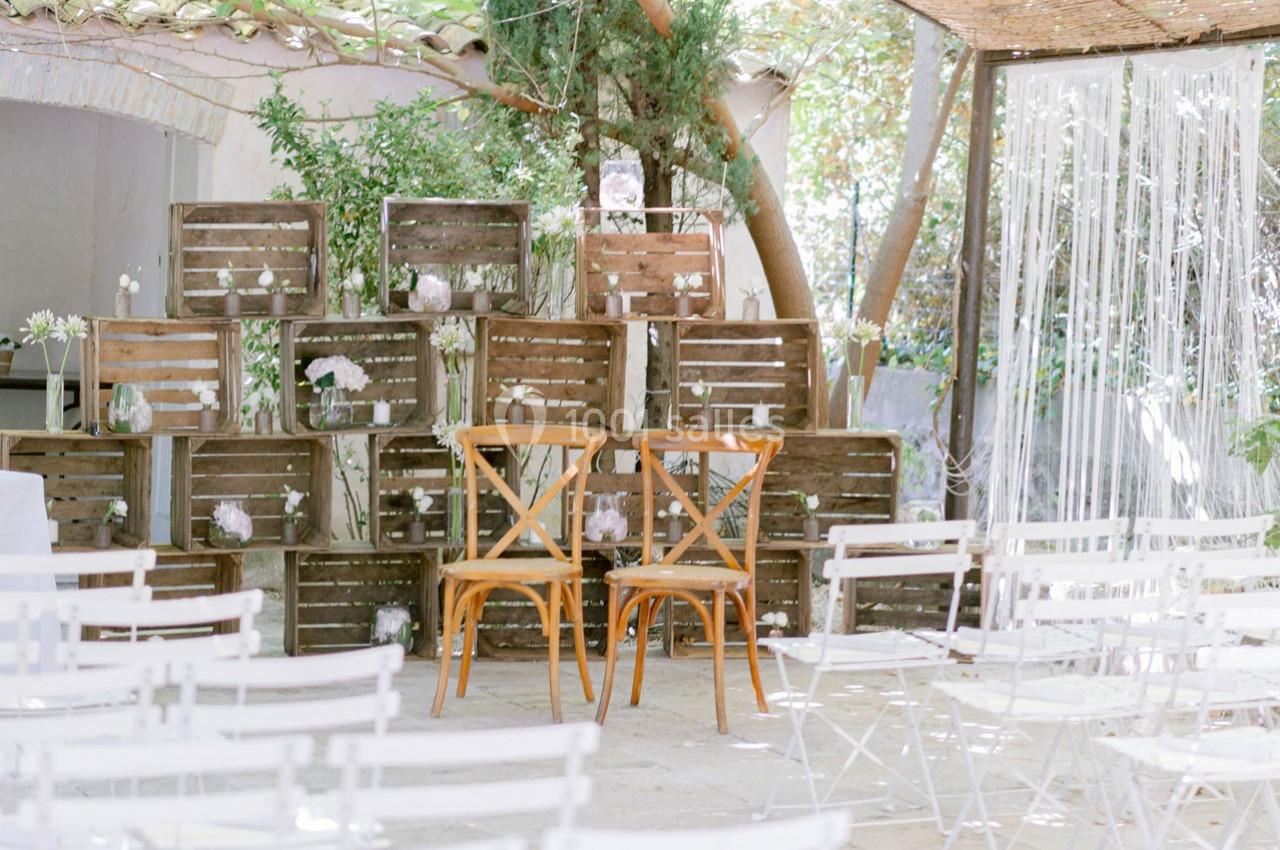 Location salle Gémenos (Bouches-du-Rhône) - Moulin de Gemenos #100 Deux chaises en bois devant un décor rustique composé de caisses en bois et de fleurs, dans un espace extérieur.