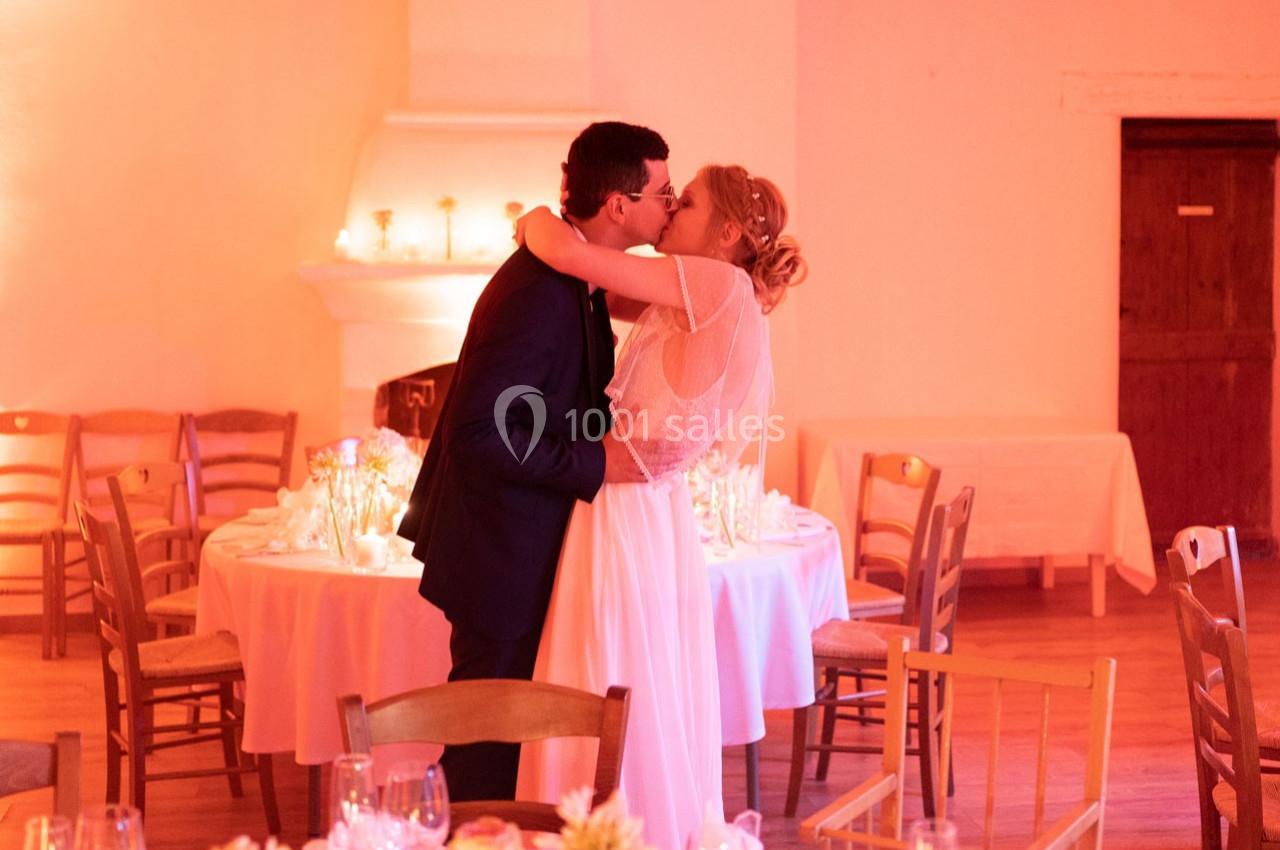 Location salle Gémenos (Bouches-du-Rhône) - Moulin de Gemenos #104 Un couple en tenue de mariage s'embrasse dans une salle décorée avec des tables et des bougies.