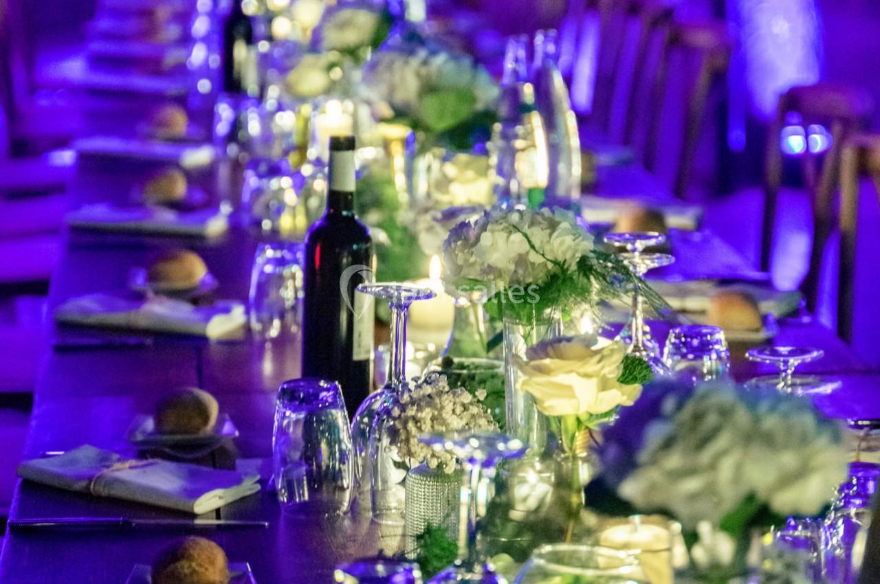Location salle Gémenos (Bouches-du-Rhône) - Moulin de Gemenos #110 Table décorée pour un dîner, ornée de fleurs blanches, verres, bougies et une bouteille de vin, éclairage tamisé.