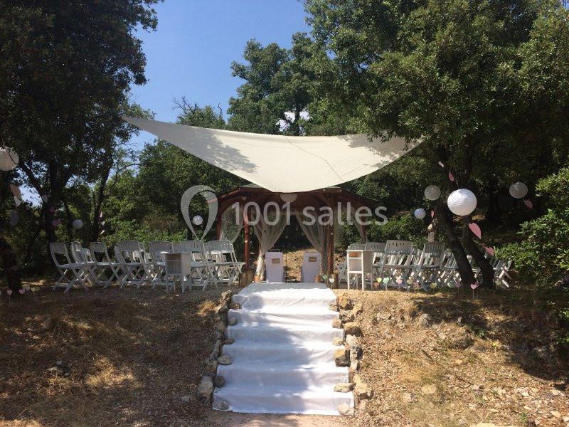 Location salle La Roquebrussanne (Var) - Les Arbousiers #15 Lieu de cérémonie en plein air avec une tonnelle décorée, des chaises blanches et une allée centrale bordée de pierres.