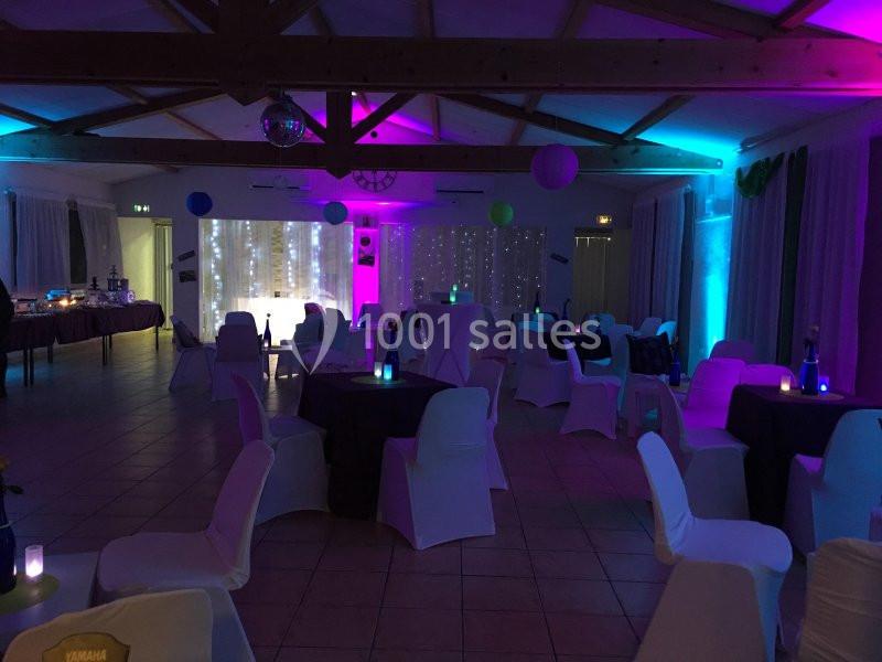 Location salle La Roquebrussanne (Var) - Les Arbousiers #35 Salle de réception décorée avec des lumières colorées, des tables et des chaises blanches sous une charpente en bois.